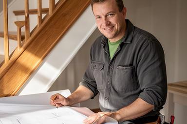 Ashton Shaghaghi reviewing a renovation plan beside a finished wood staircase